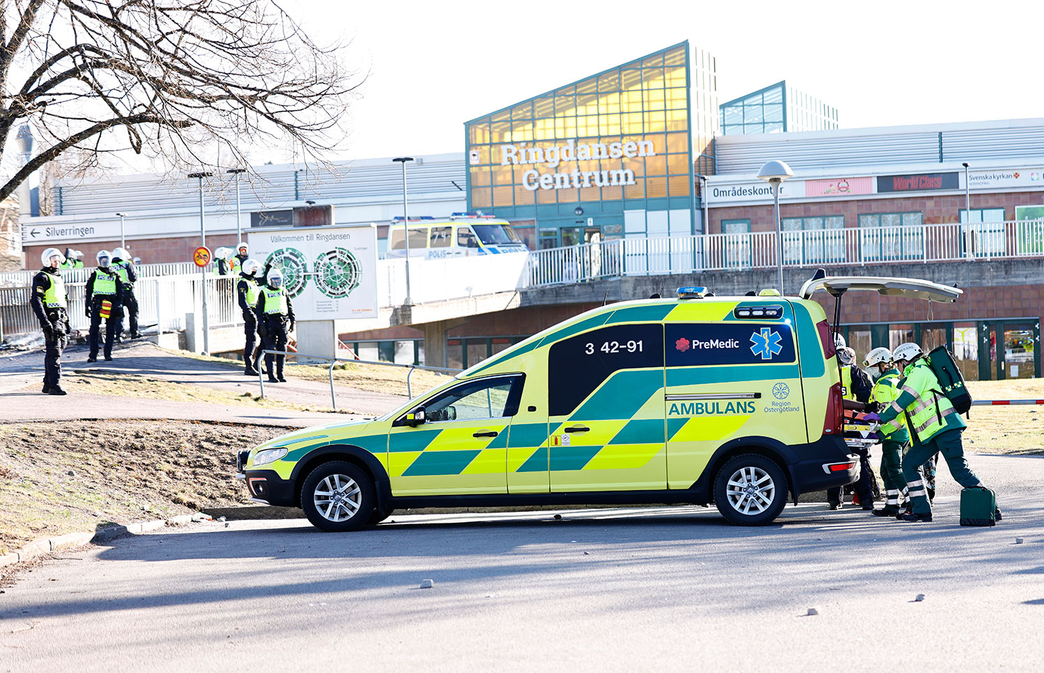 En mann som er skutt i beinet, tas hånd om av politi og ambulansepersonell.